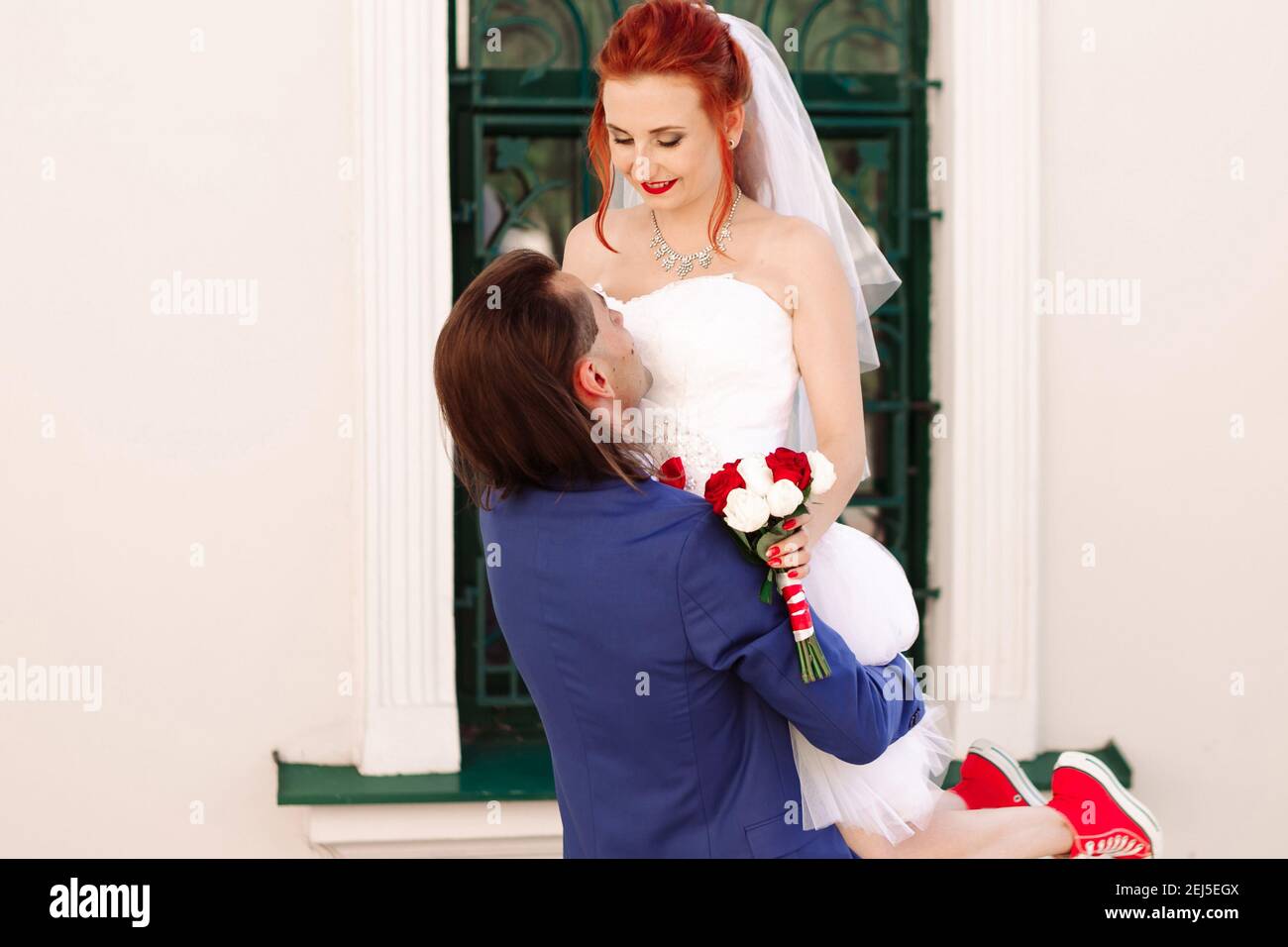 Retrato de la joven novia y novio. El joven sostiene a una novia con ramo  de rosas. Mujer con zapatillas rojas y vestido blanco – concepto de boda de  cintura baja Fotografía