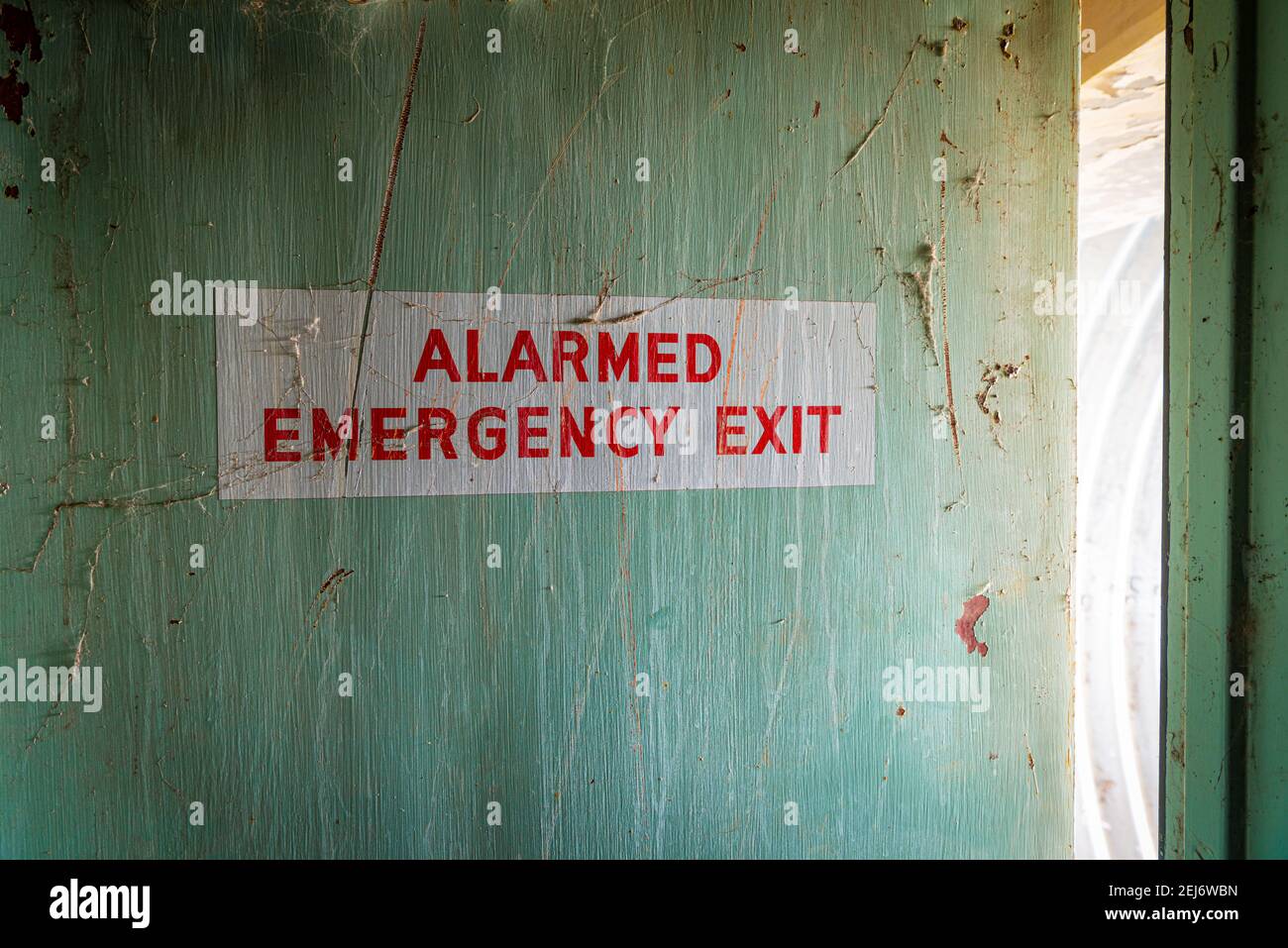 Interior de una puerta de salida de emergencia pintada. La puerta está en mal estado de reparación y tiene un color y una textura interesantes. Foto de stock