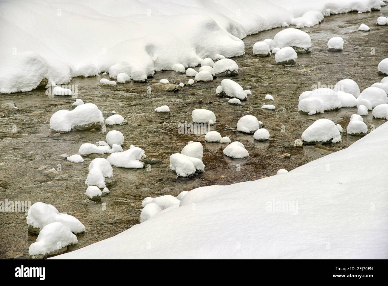 Río de montaña congelado con hielo que fluye cerca de las costas nevadas en frío día de invierno en el campo Foto de stock