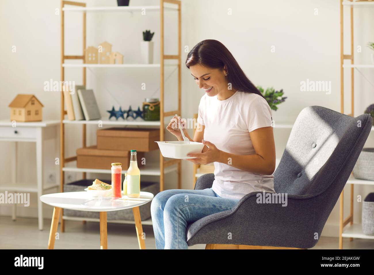 Feliz mujer joven sonriente con comida sana para llevar sentada un sillón en casa Foto de stock