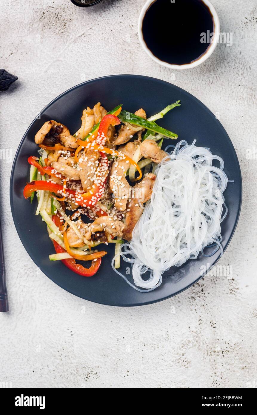 Carne de pollo con verduras wok y fideos de arroz chino, salsas y sésamo en  un tazón negro con palillos chinos de fondo gris claro. Traditi Fotografía  de stock - Alamy