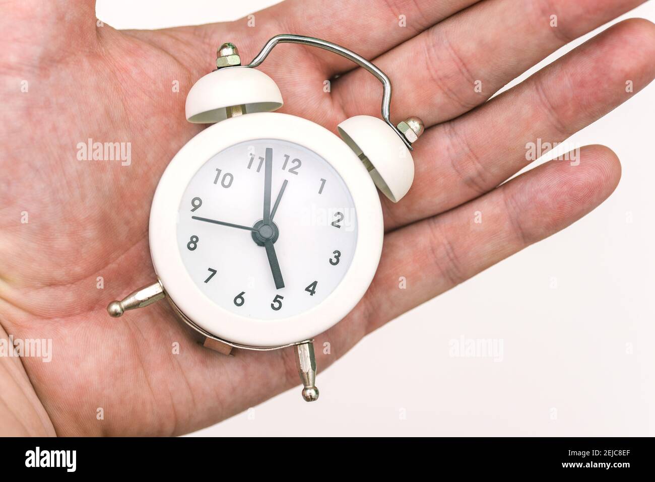 Las manos de la hora muestran las cinco de la mañana o de la noche. Fin de  la jornada laboral. Duración del trabajo. Concepto de tiempo. Despertador  en la palma de un