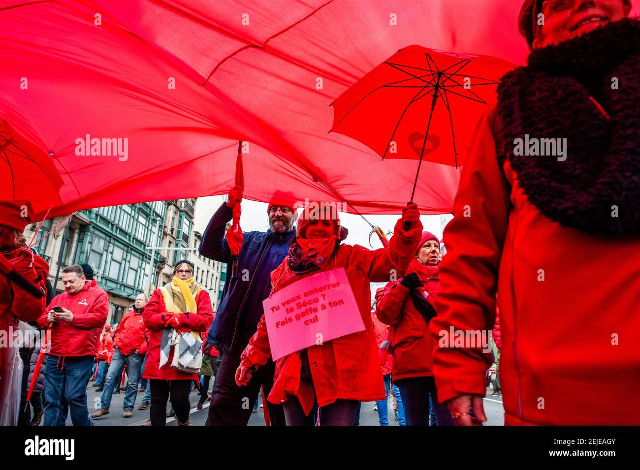 Una mujer camina bajo una enorme bandera roja mientras sostiene un paraguas  rojo durante la manifestación en Bruselas. El sindicato socialista ABVV  organizó una manifestación nacional para una seguridad social fuerte y
