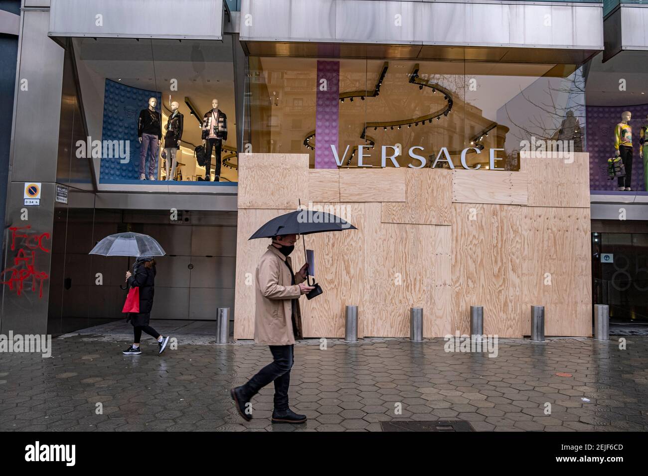Barcelona, España. 22 febrero de 2021. Un hombre que sostiene un paraguas pasa por la tienda Versace en Passeig Gràcia visto con protecciones contra el vandalismo en sus ventanas.más