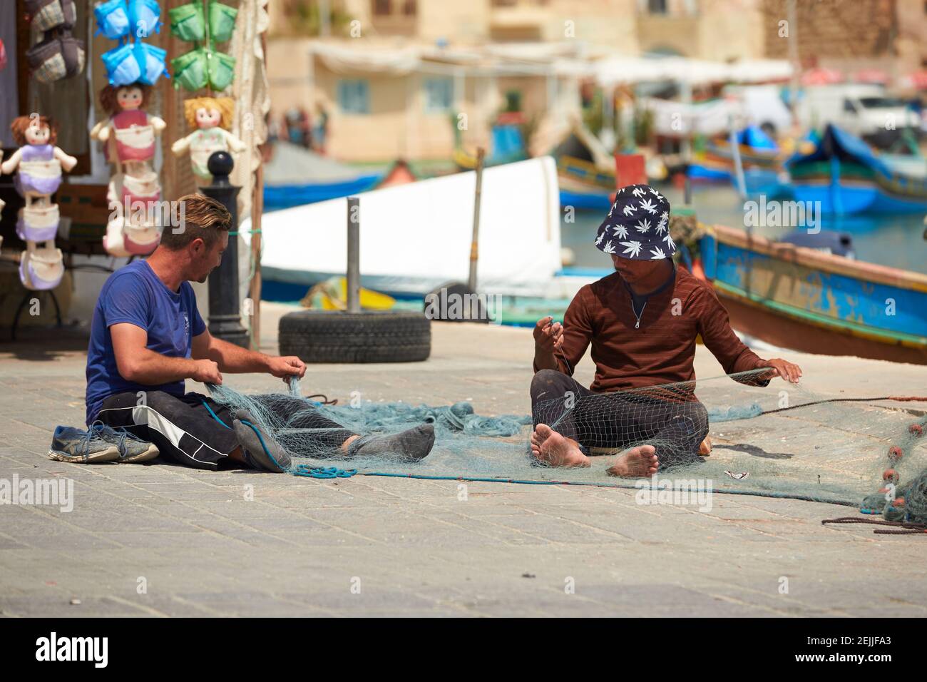 Pescadores reparando redes contra un fondo de color. Escena de las calles de la Valeta, Malta. Foto de stock