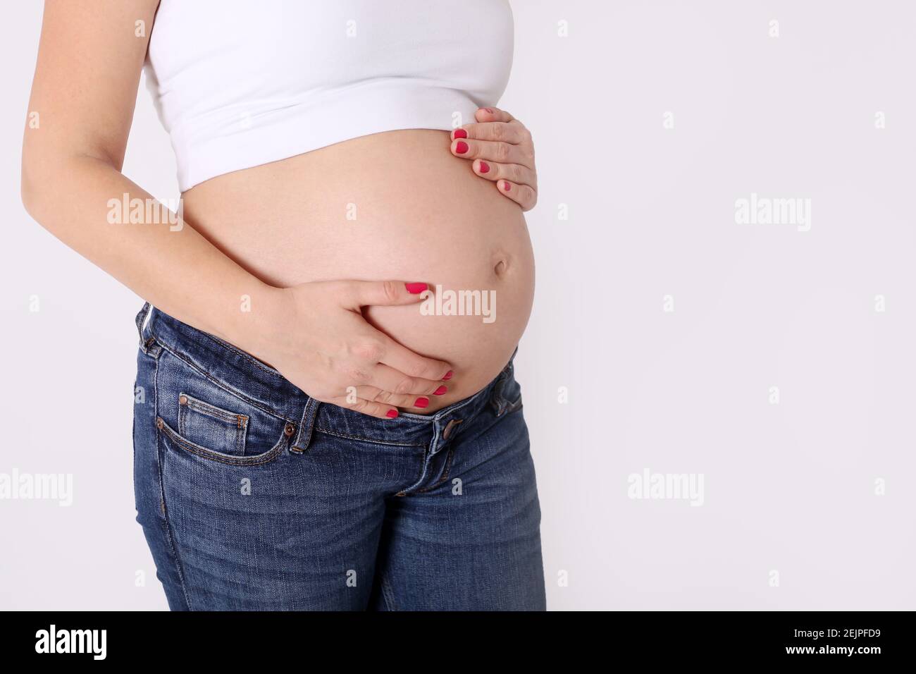 Mujer embarazada en jeans y la parte superior blanca de mantener las manos  su vientre Fotografía de stock - Alamy