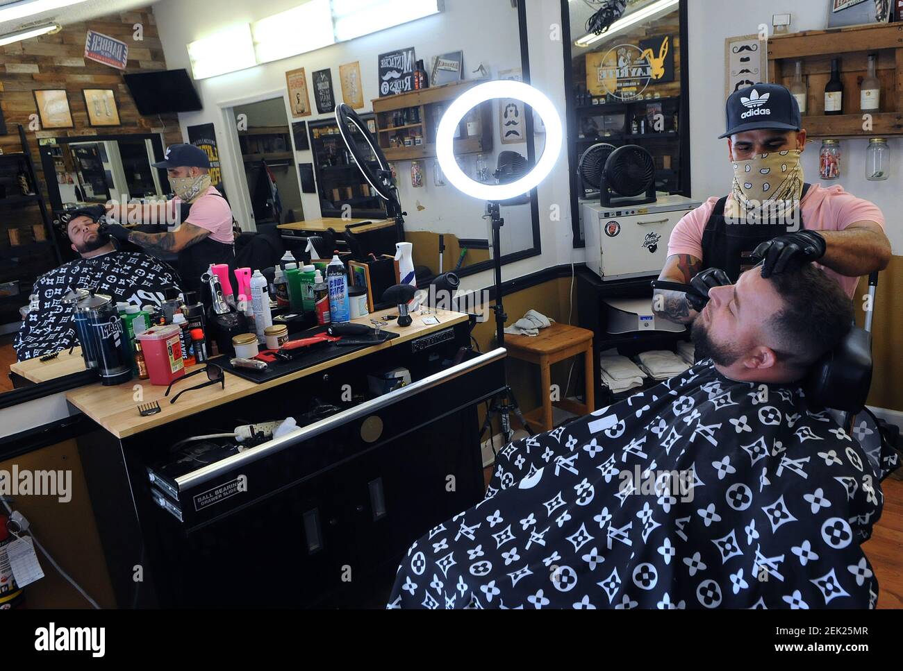 Luis Lugo recorta la barba de Lenny Iacommare en Hair Godz Studios el  primer día en que se permitió reabrir tiendas de barbería y salones en  Florida en medio de la pandemia