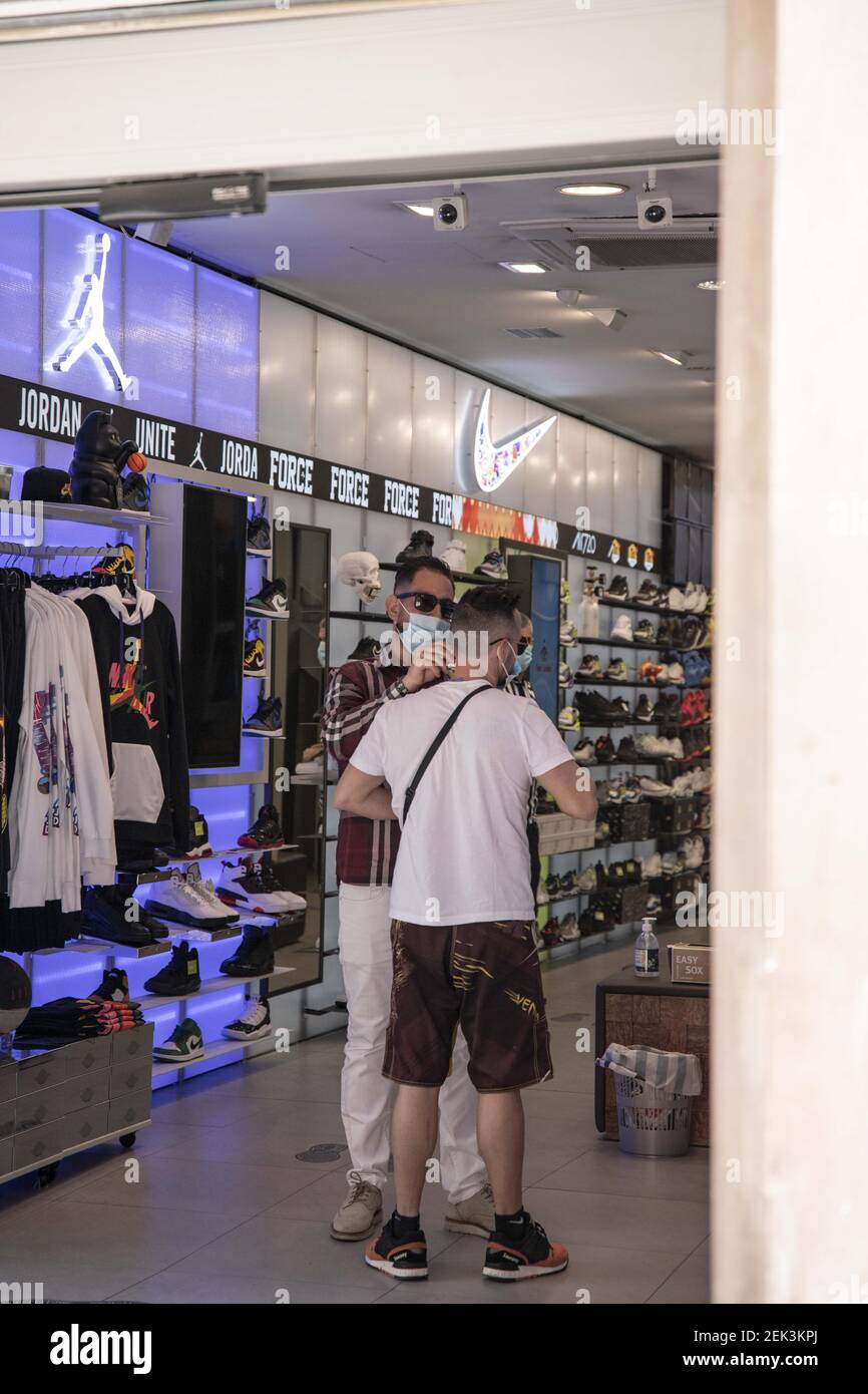Un hombre ayuda a su compañero a poner la máscara obligatoria en una tienda  de ropa en el centro de la zona comercial Portal del Angel en Barcelona,  España el 24 de