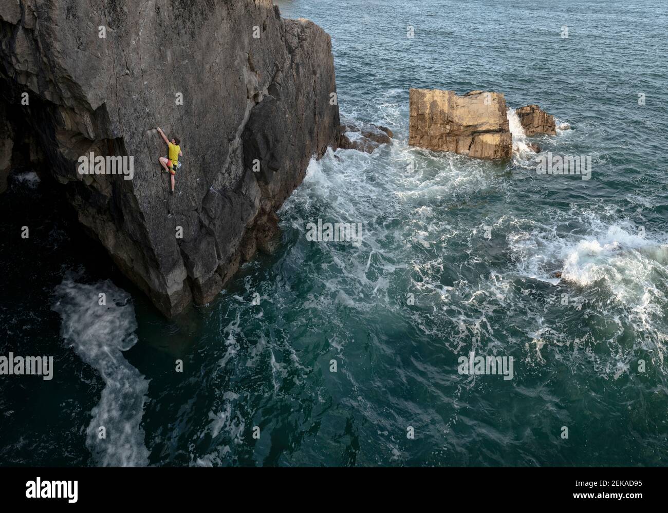Joven escalador de roca macho escalando acantilado contra el mar Foto de stock