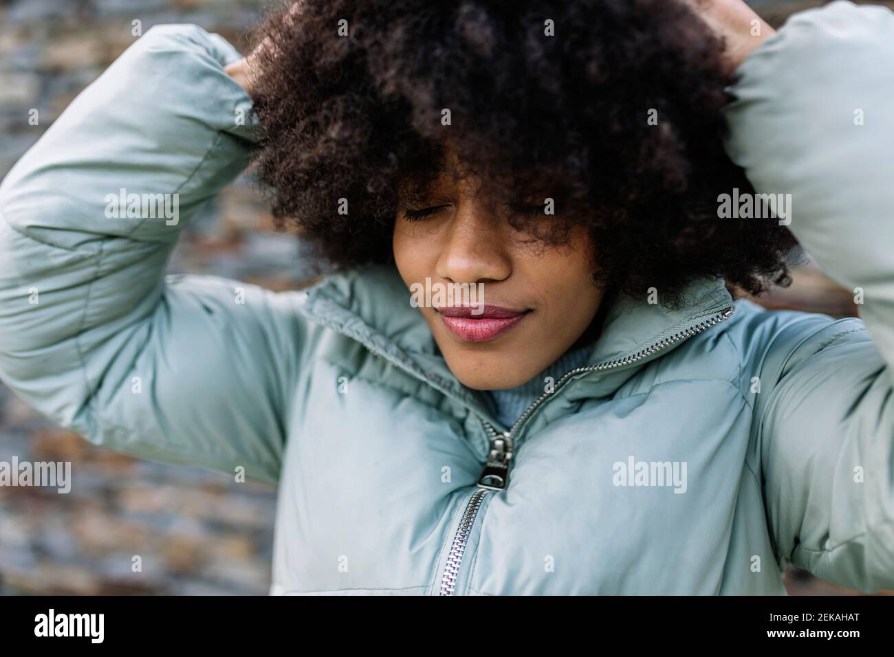 Mujer afro con la mano en el cabello y los ojos cerrados al aire libre Foto de stock
