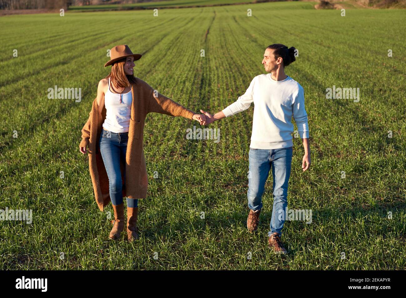 Pareja heterosexual con la mano mirando el uno al otro mientras caminar por la tierra verde Foto de stock