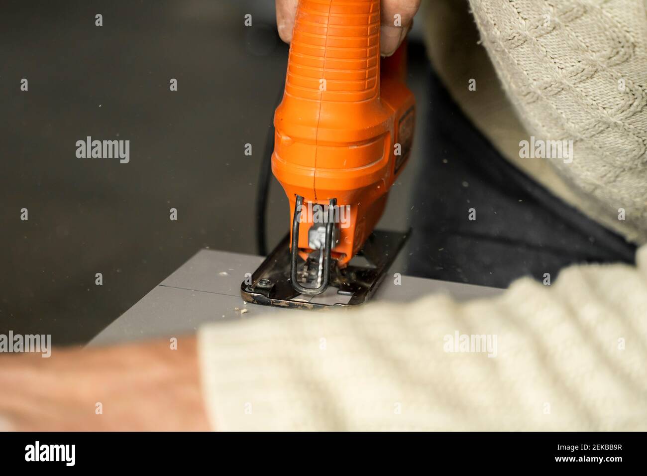 Hombre mano usando sierra de calar eléctrica para cortar una fibra de  madera en la parte trasera de un armario de cocina a medida. Instalación de  la cocina. Carpintero con un Fotografía