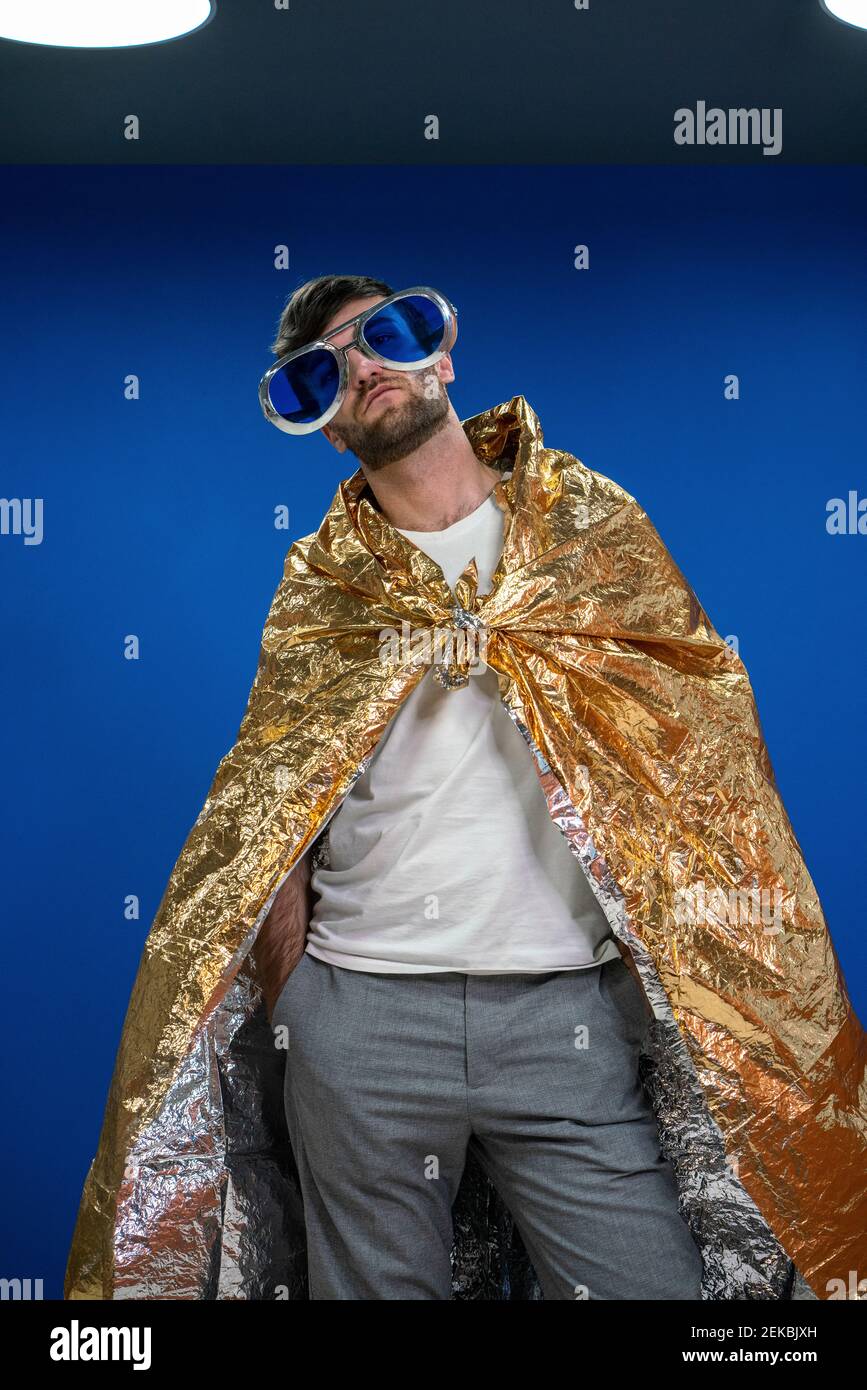 Hombre emprendedor en gafas de novedad con papel para envolver de color  dorado capa contra pared azul en el lugar de trabajo Fotografía de stock -  Alamy