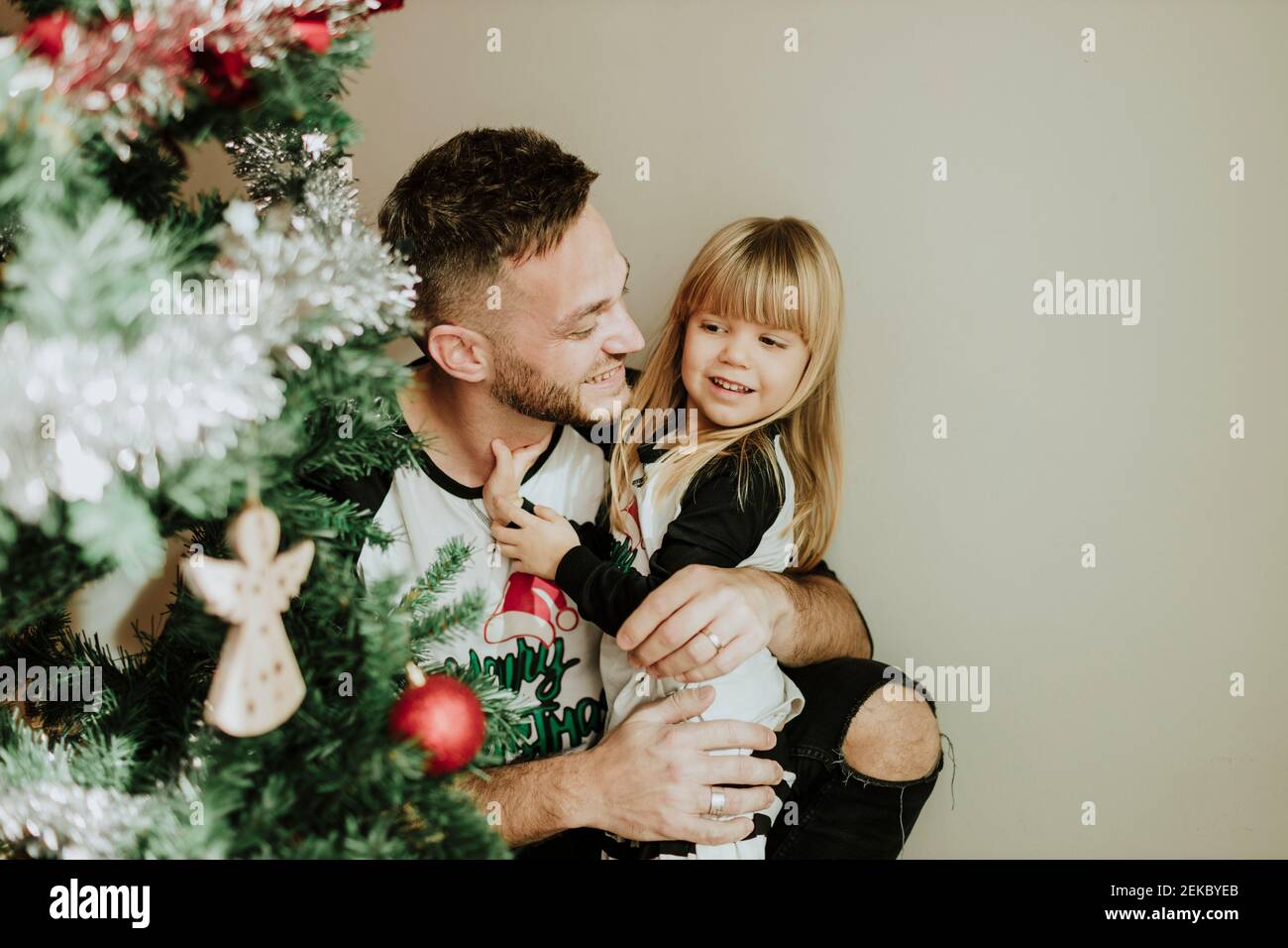 Padre sonriente sosteniendo la mano de su hija junto al Árbol de Navidad en casa Foto de stock