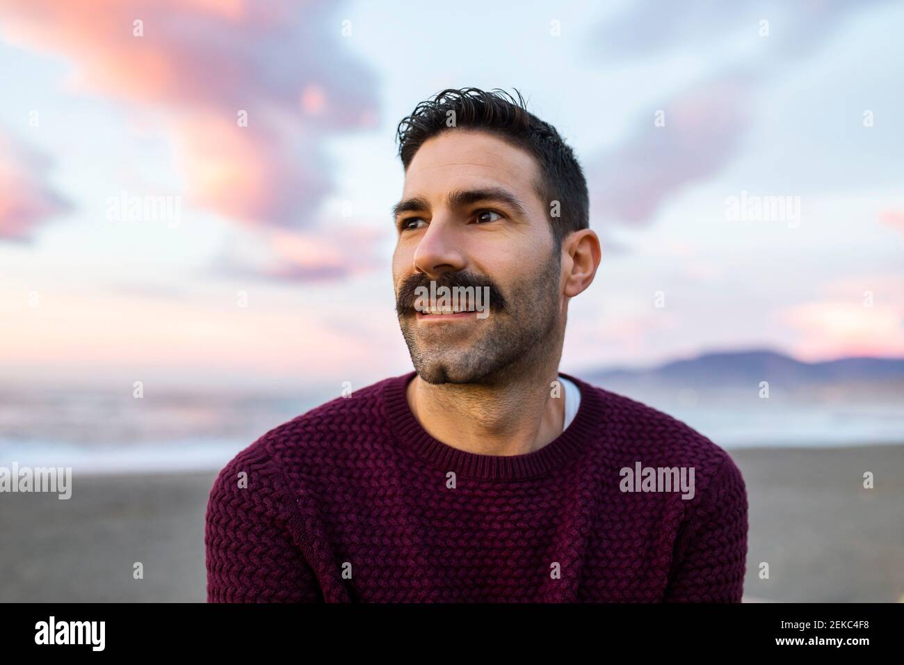 Un hombre guapo en un día de suéter maroon soñando en la playa durante  amanecer Fotografía de stock - Alamy