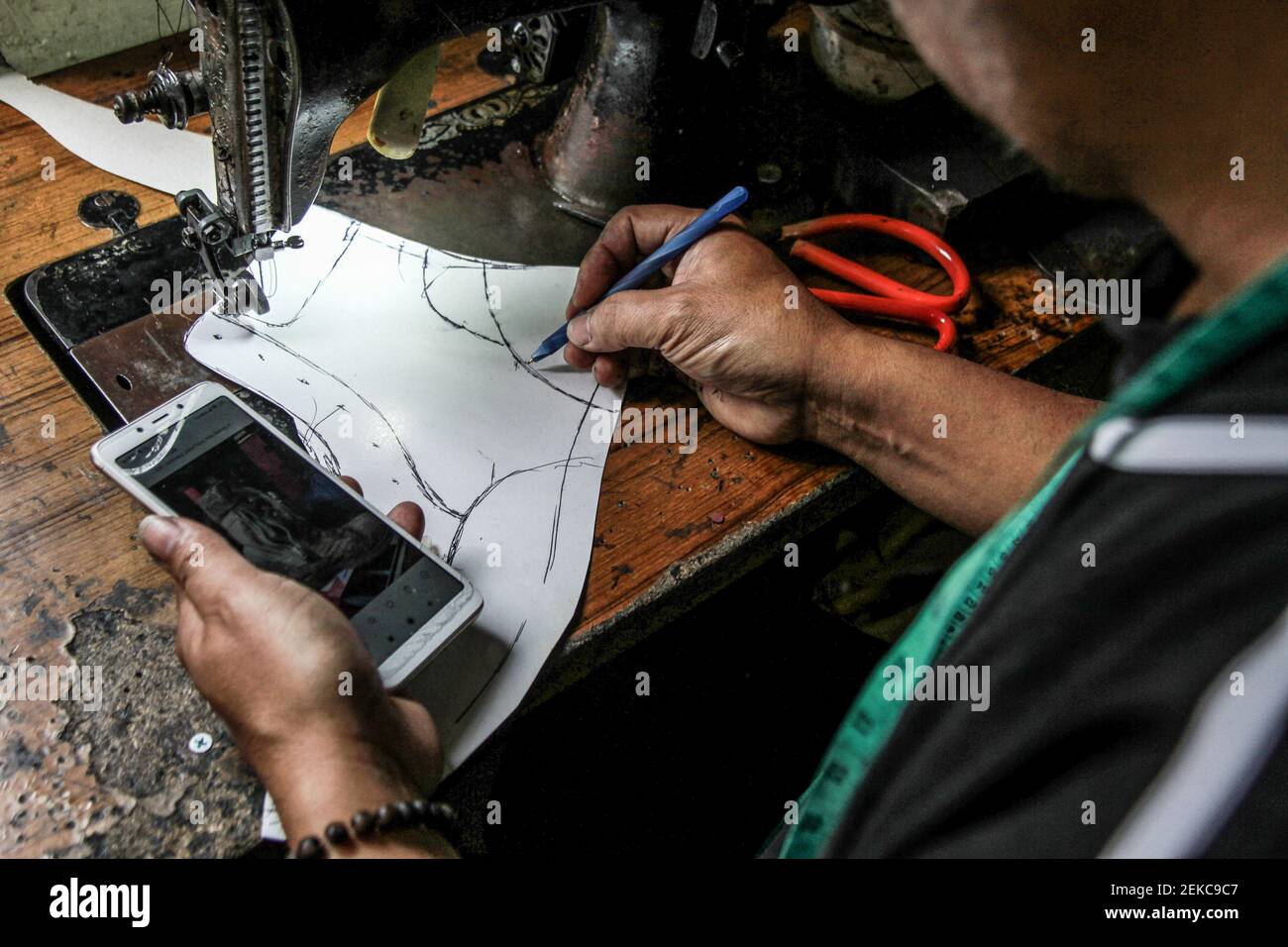 Un zapatero en su taller en Malang vio trabajar en un proyecto mientras  sostenía el teléfono. Rini, el dueño de la zapatería se ve obligado a hacer  la promoción y las ventas
