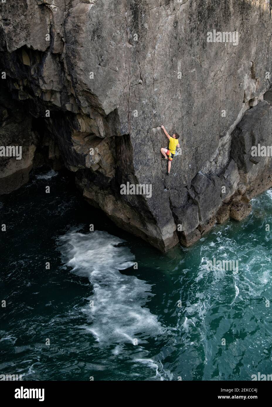 Joven hombre escalador de roca escalando acantilado sobre el agua Foto de stock