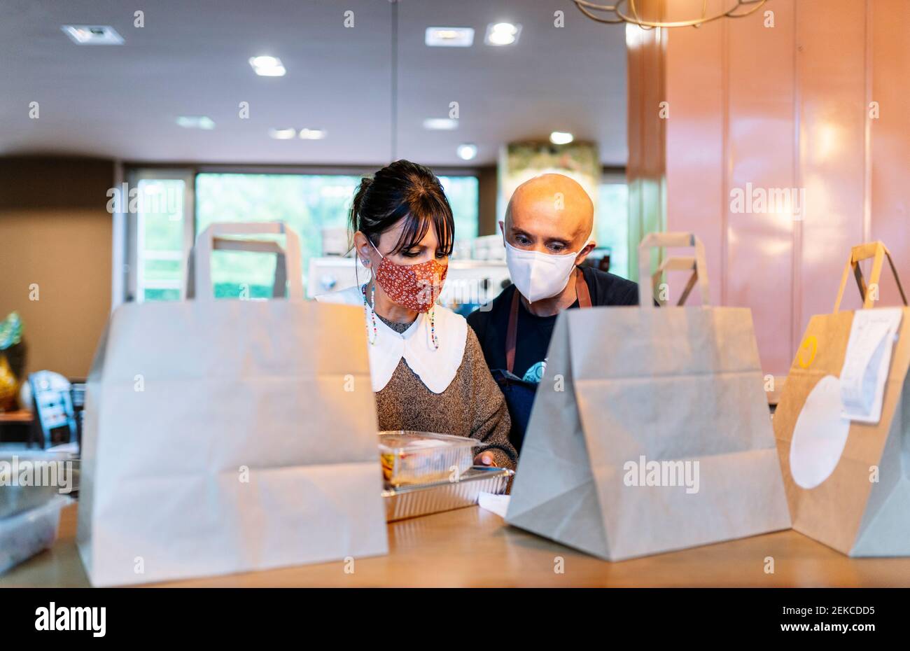 Mujer propietaria con un colega que prepara comida para llevar barra de barra durante la pandemia Foto de stock