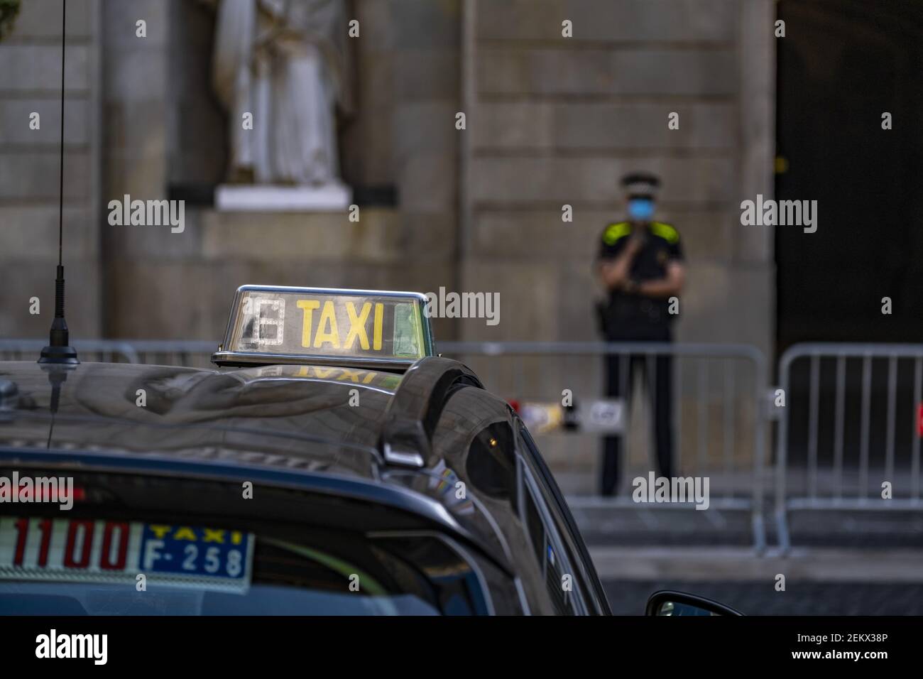 El indicador de LUZ DE TAXI en el techo de un vehículo se ve frente a la  entrada del Ayuntamiento de Barcelona, custodiado por un agente de la  Guardia Urbana de Barcelona.