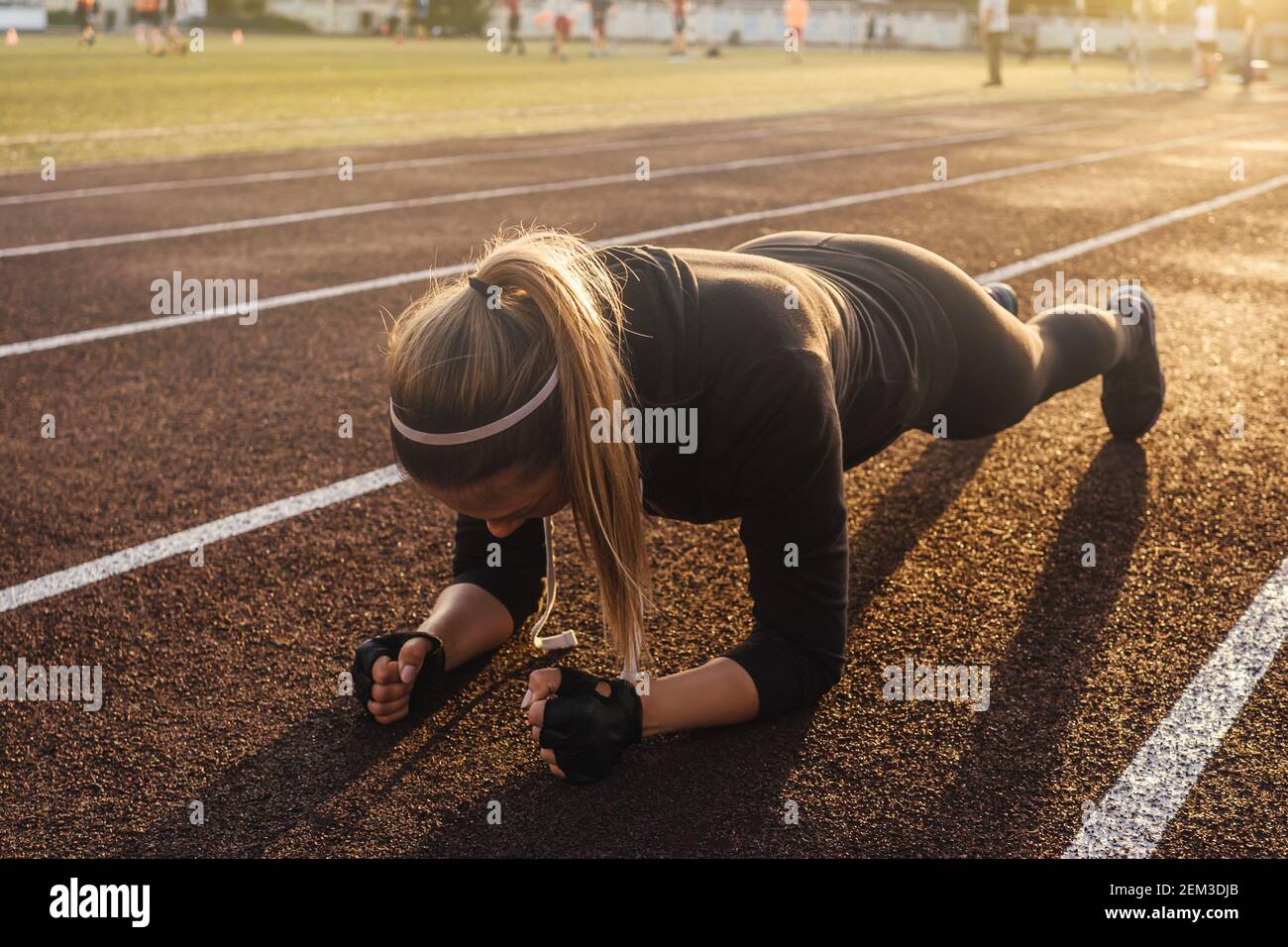 Joven mujer atlética haciendo ejercicio de tabla en pista de correr. Luz de puesta de sol sobre fondo, hermosa perspectiva. Foto de stock