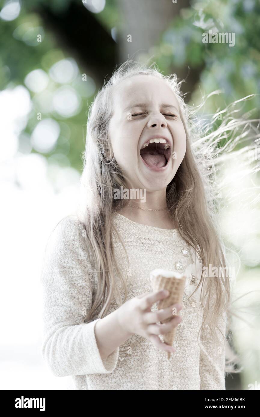 Helado le hace caer en la euforia. Cute Little Girl comer helado en verano.  Niño pequeño lamiendo el cono de helado en el exterior. Adorable niño feliz  disfrutando de postre cremoso helado