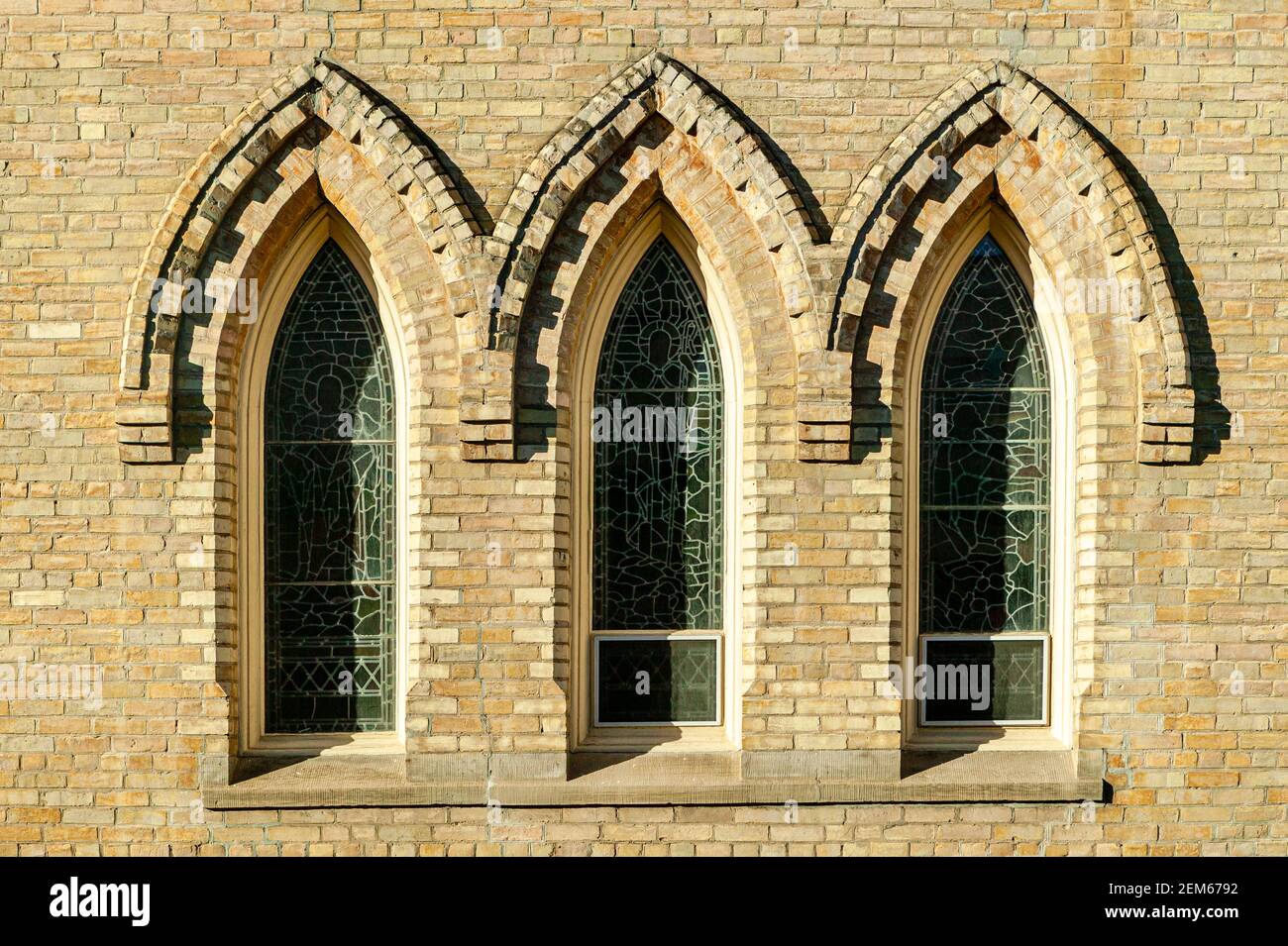 Un conjunto de ventanas de vidrio con plomo enmarcadas con detalles de ladrillo en una iglesia en Ontario. Foto de stock