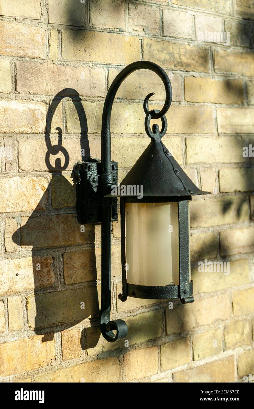 Un viejo accesorio de iluminación de hierro forjado hecho a mano en una pared de ladrillo de color cálido. Foto de stock