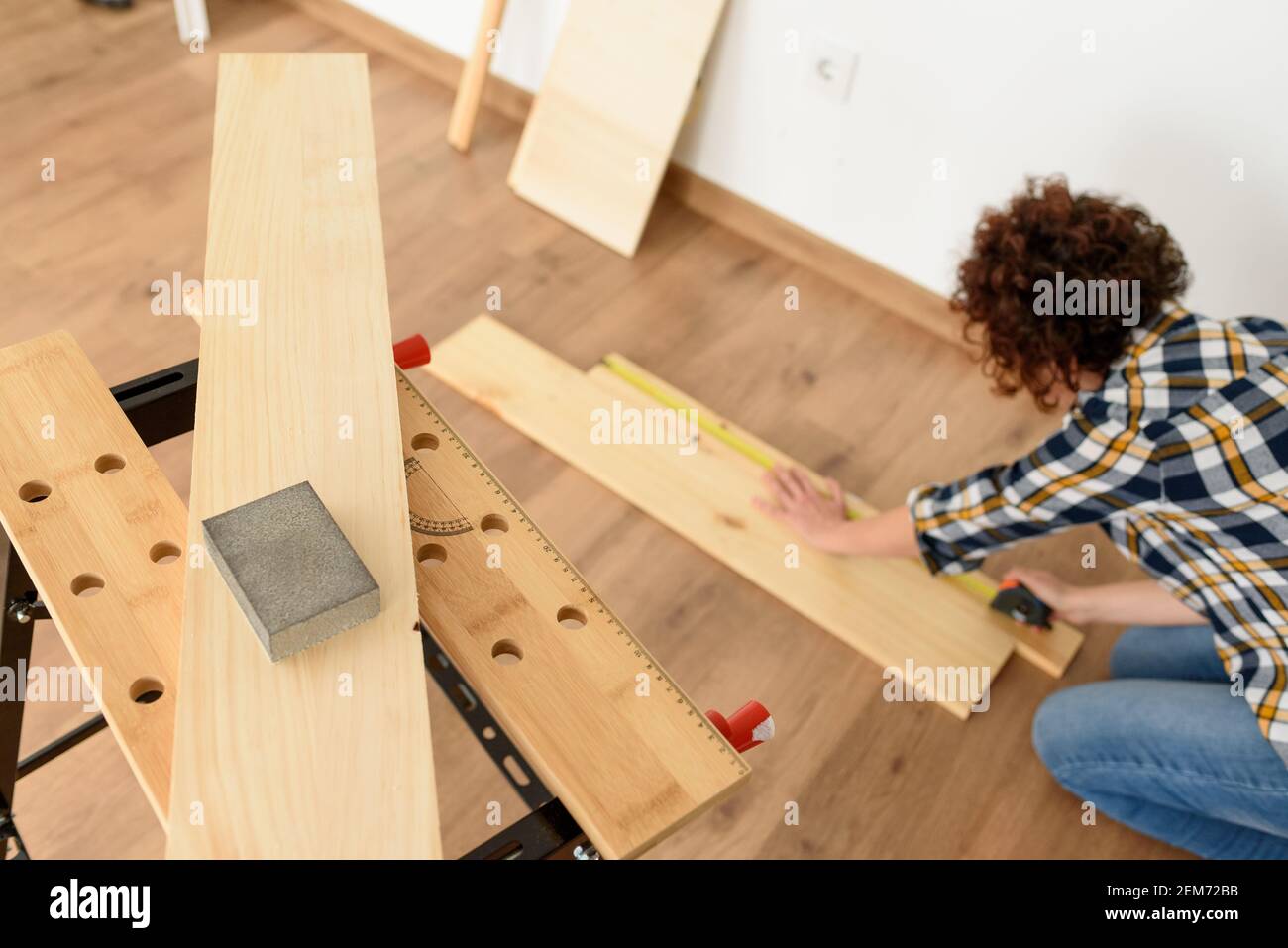 Primer plano de un papel de lija de madera en un banco de trabajo con una mujer trabajando en el fondo. Disparo en interiores. Luz natural. Foto de stock
