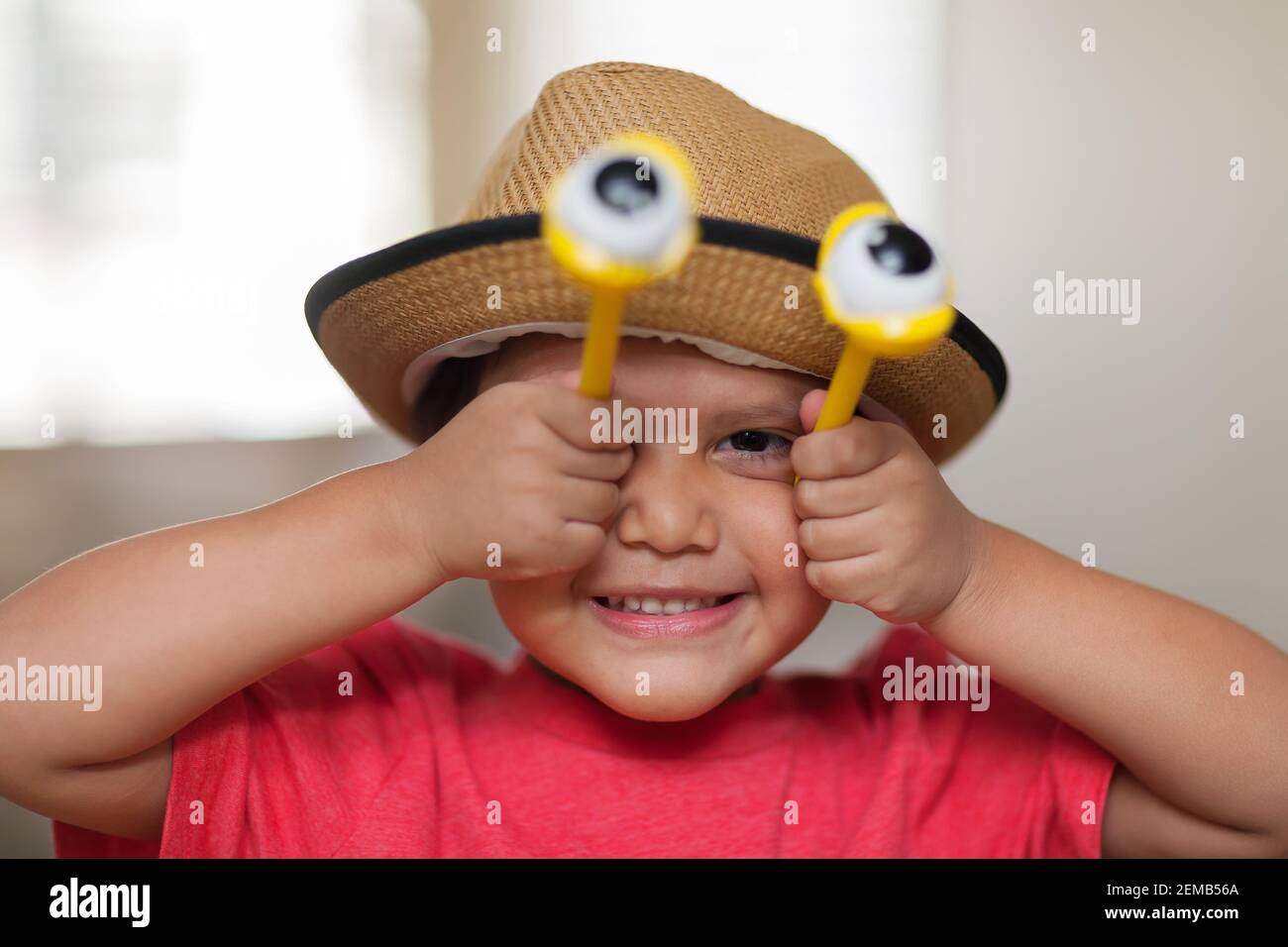 Un niño latino imaginativo que se divierte y juega con ojos de insecto, fingiendo ser insecto, de cuatro años y usando un sombrero para niños. Foto de stock