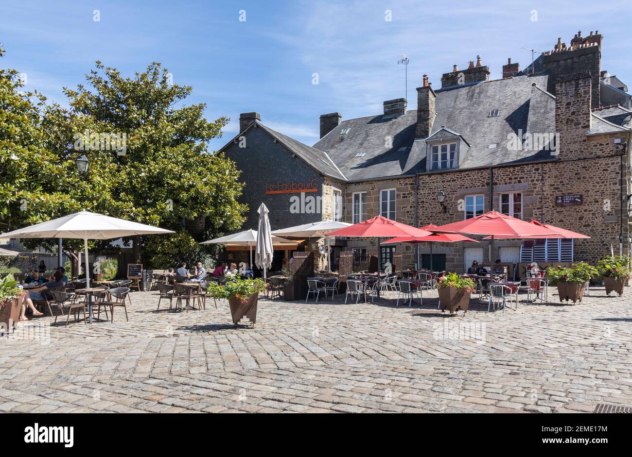 La gente se relaja en un café al aire libre en Fougeres, Francia, disfrutando del sol brillante de verano bajo la sombra de los paraguas de colores rodeados de edificios Foto de stock
