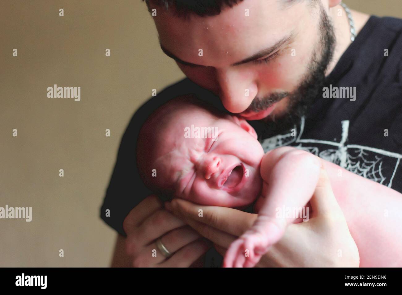 Papá sostiene a un recién nacido llorando en sus brazos y besos tiernamente Foto de stock