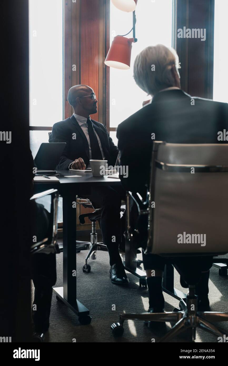 Hombres profesionales mirando fuera mientras que se sentaba en la mesa de la conferencia adentro sala de juntas durante la reunión Foto de stock