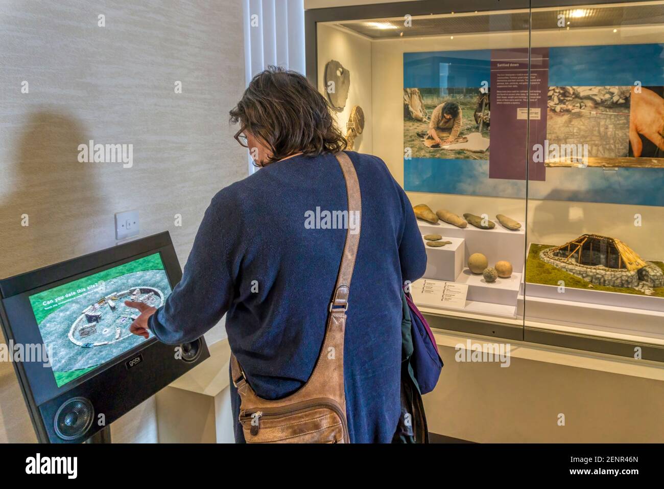 Mujer usando un panel táctil interactivo para leer más información como parte de una exhibición del museo. Foto de stock