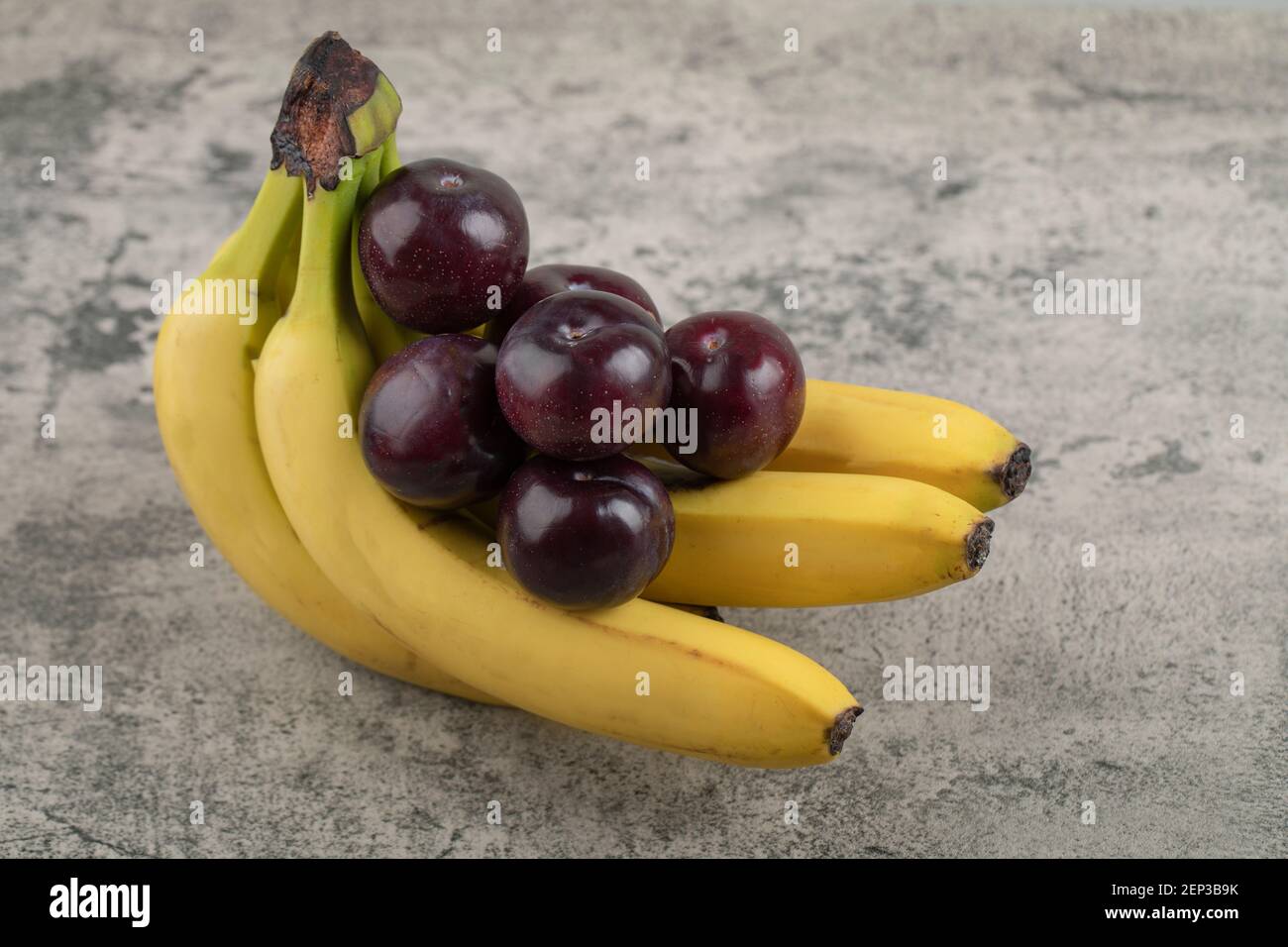 Ciruelas frescas y saludables con racimos de plátano sobre fondo de piedra Foto de stock