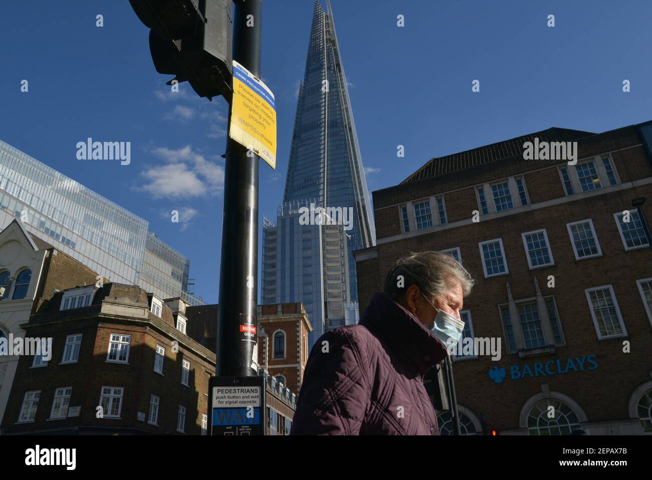 Una mujer que lleva una máscara facial como protección contra el coronavirus (covid-19) pasa por el rascacielos de Shard en London Bridge, Londres, Reino Unido Foto de stock