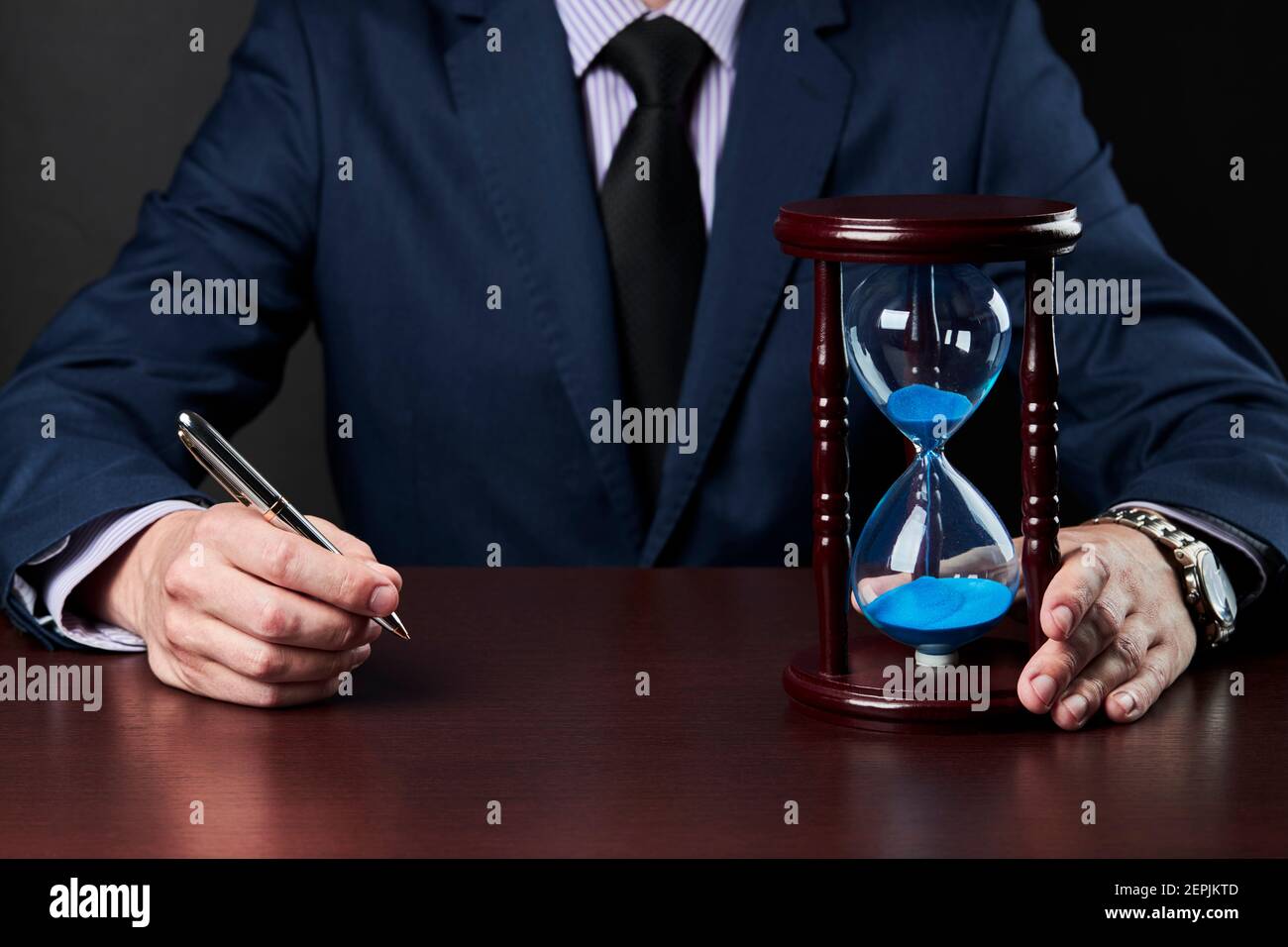 hombre de negocios sosteniendo el lápiz en el brazo y reloj de arena de pie sobre una mesa. concepto de fecha límite Foto de stock