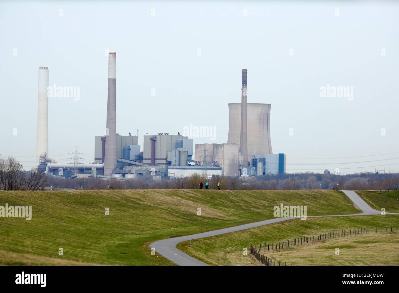 Von Duisburg Walsum aus schaut man auf das stillgelegte Kraftwerk Voerde. Im Vordergrund fahren 3 Personen Fahrrad auf dem Rheindeich. Es ist ein grau Foto de stock