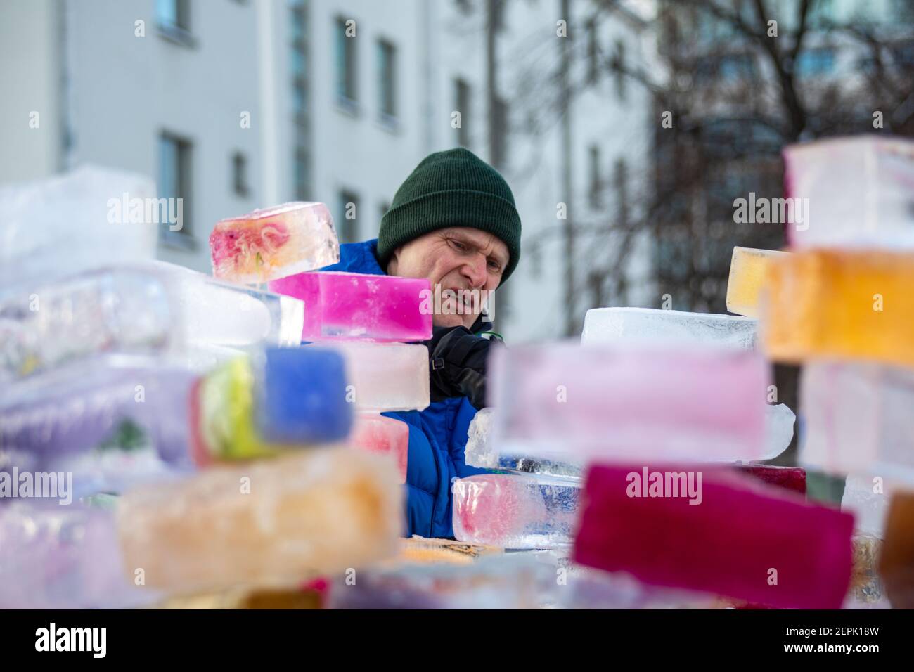 Hombre que participa en un proyecto comunitario de construcción de un castillo de hielo o fortaleza a partir de ladrillos o bloques de hielo de colores en Munkkiniemi, Helsinki, Finlandia Foto de stock