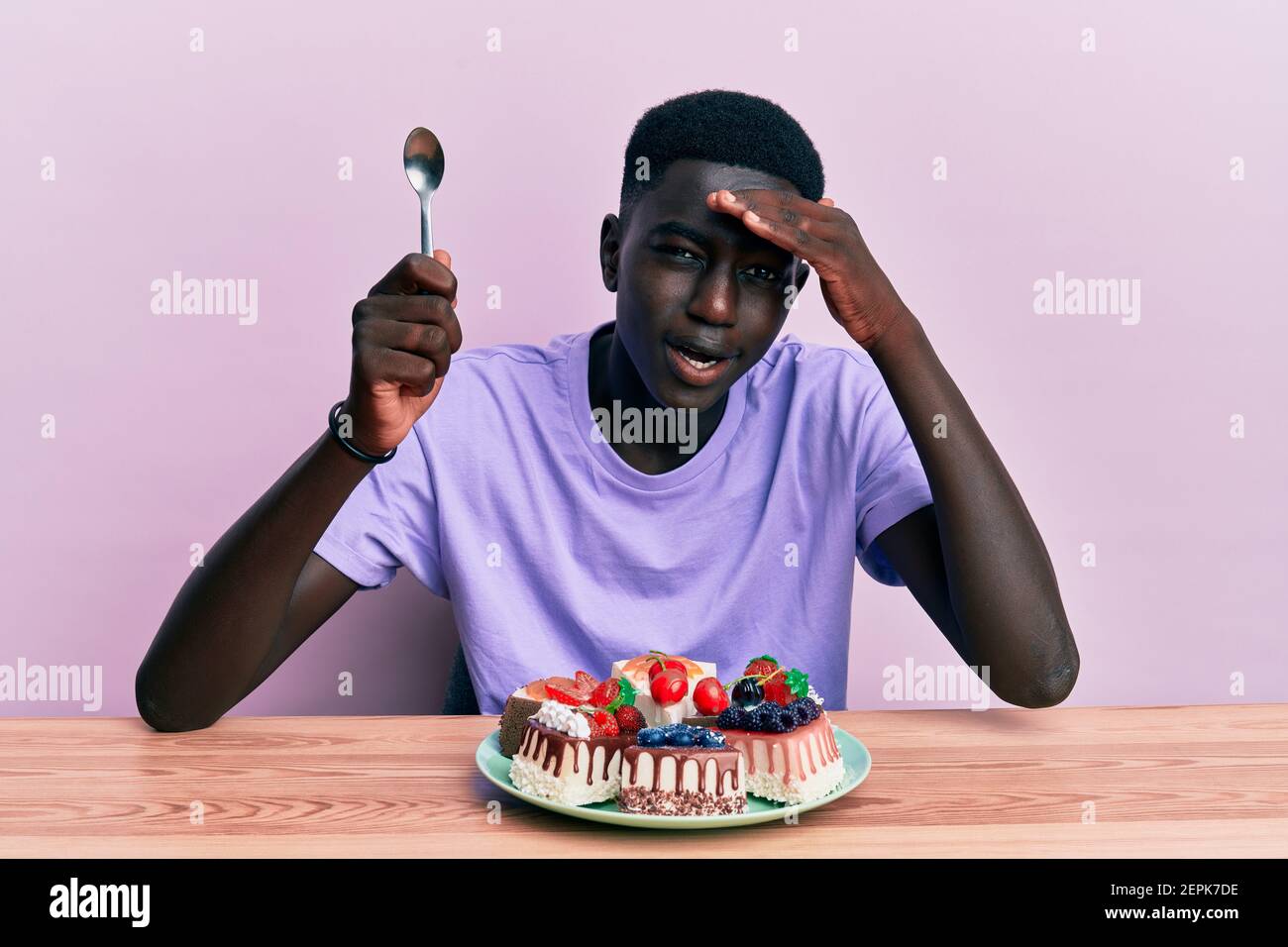 Joven afroamericano sentado en la mesa comiendo pasteles estresados y  frustrados con la mano en la cabeza, cara sorprendida y enojada Fotografía  de stock - Alamy