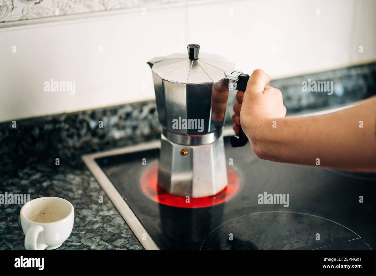 La persona de la cosecha que sostiene la estufa metal encima de la cafetera  con el plástico mango de cocina moderna en la cocina de la casa durante la  luz del día