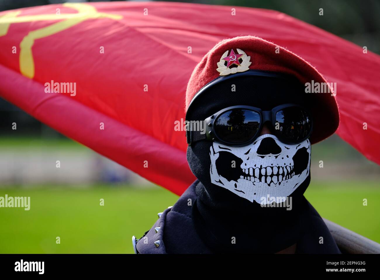 Un hombre que lleva una máscara sostiene una bandera comunista mientras la  gente se reúne en el Parque de la Península para la marcha Anual de los  niños por la Justicia Social