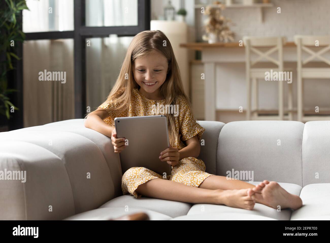 Chica sonriente sentada en el sofá leer libro en el ordenador de la tableta Foto de stock