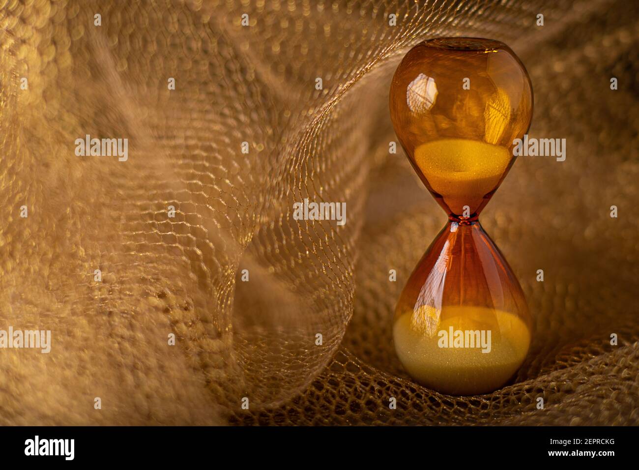 Reloj de vidrio de reloj de arena marrón sobre fondo de celosía de panal de oro. El concepto de la transición del tiempo de caducidad es valor. Primer plano con espacio de copia. Foto de stock