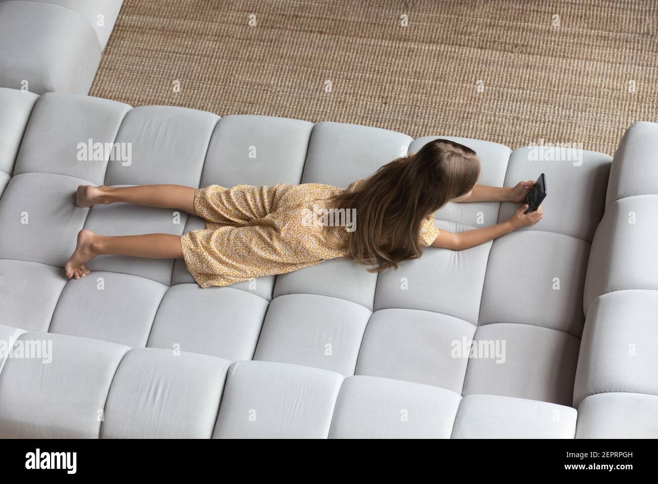Vista superior de una niña tumbada en el sofá usando la celda Foto de stock