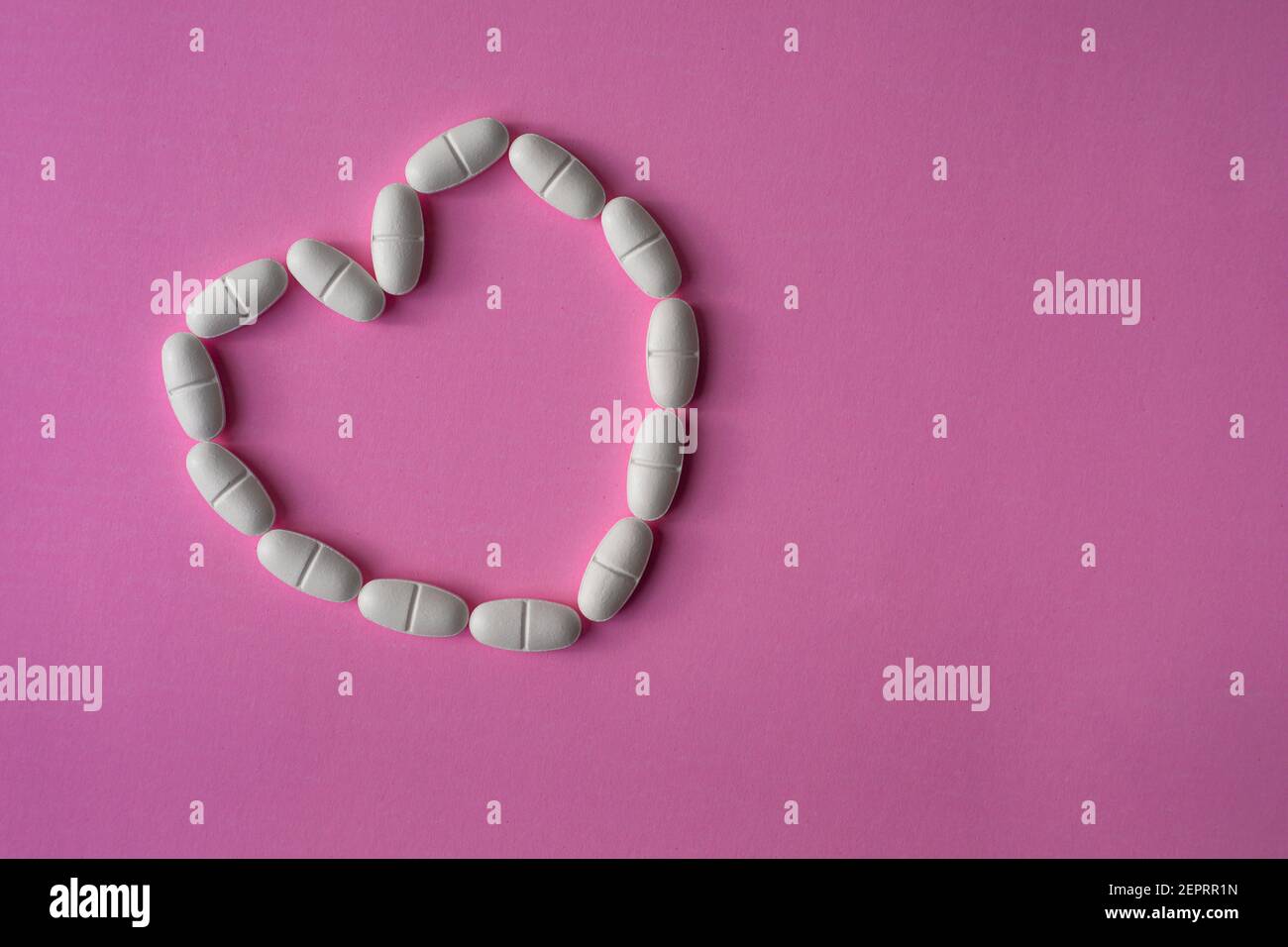 Pastillas o tabletas blancas y grandes, dispuestas en forma de corazón para representar la salud sobre fondo rosa Foto de stock