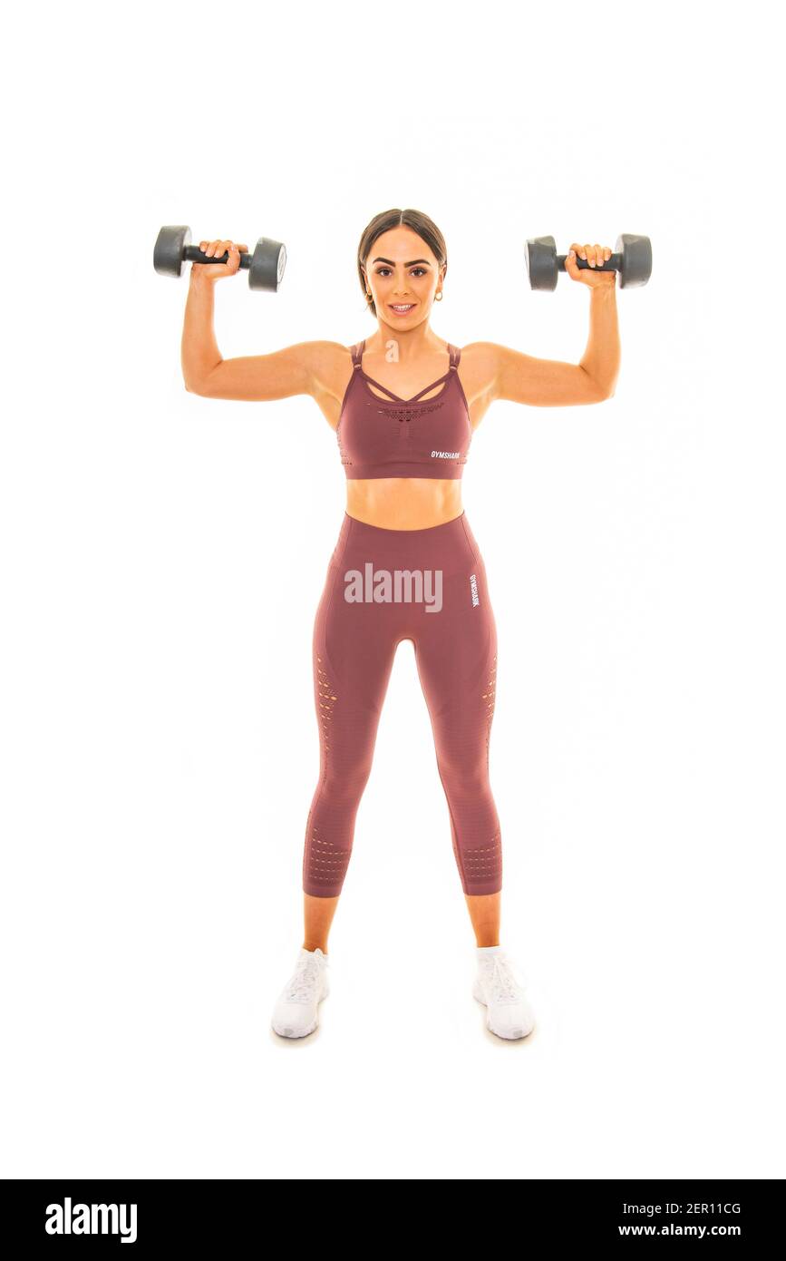 Retrato vertical de una joven usando pesas en un entrenamiento, aislado sobre un fondo blanco. Foto de stock