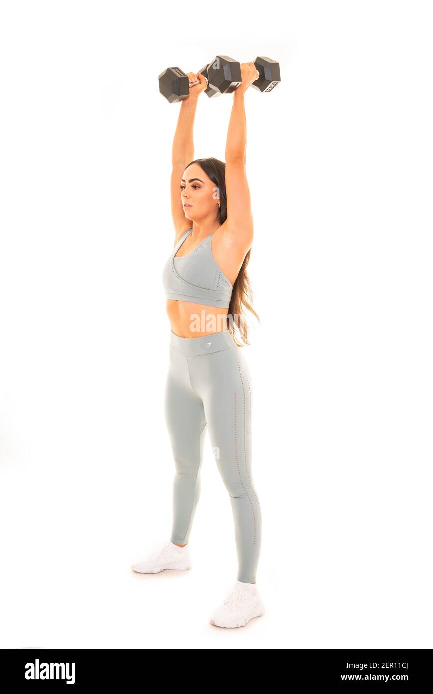 Retrato vertical de una joven usando pesas en un entrenamiento, aislado sobre un fondo blanco. Foto de stock