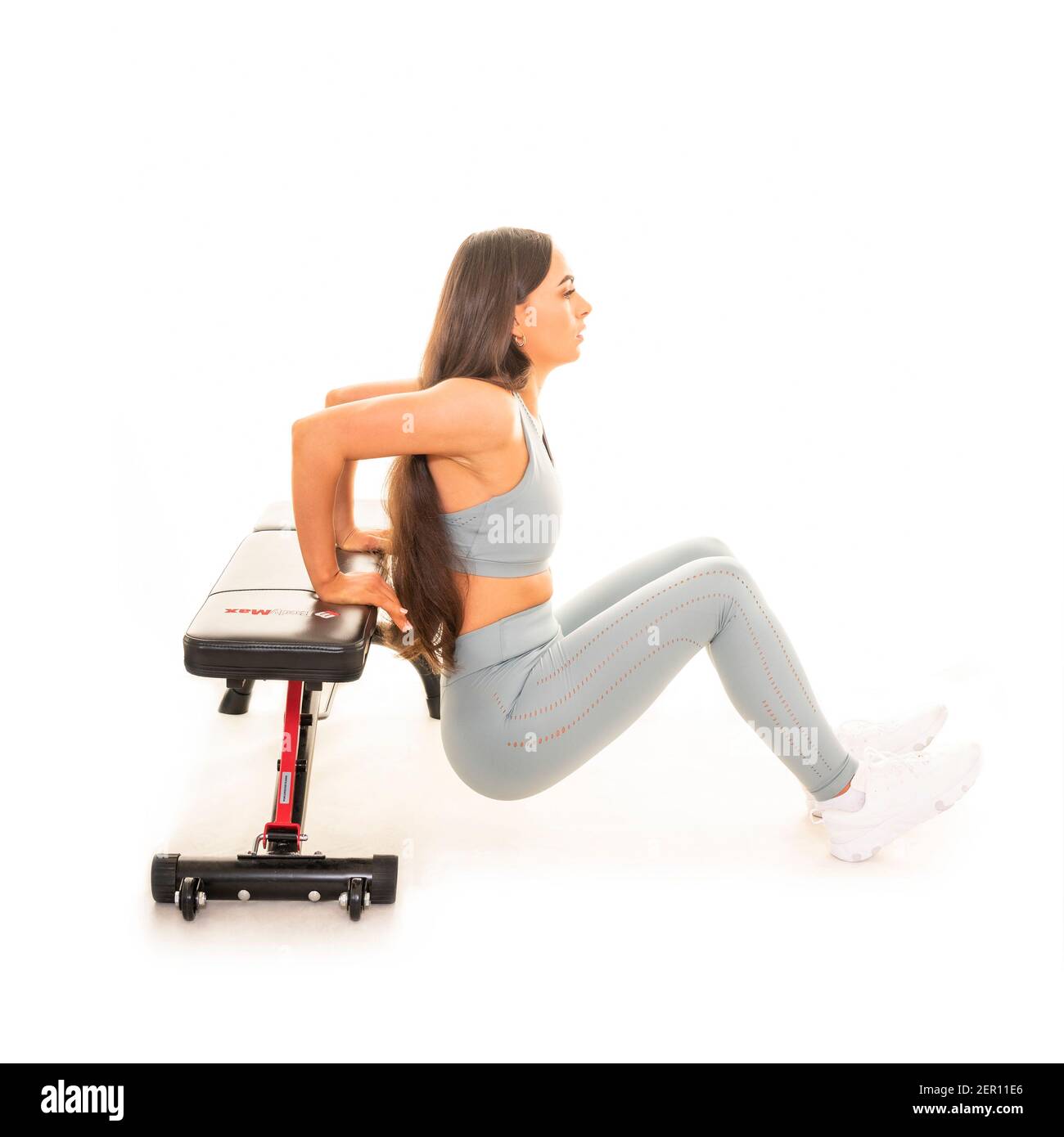 Retrato cuadrado de una mujer joven haciendo un descenso de tríceps usando un banco de gimnasio, aislado sobre un fondo blanco. Foto de stock