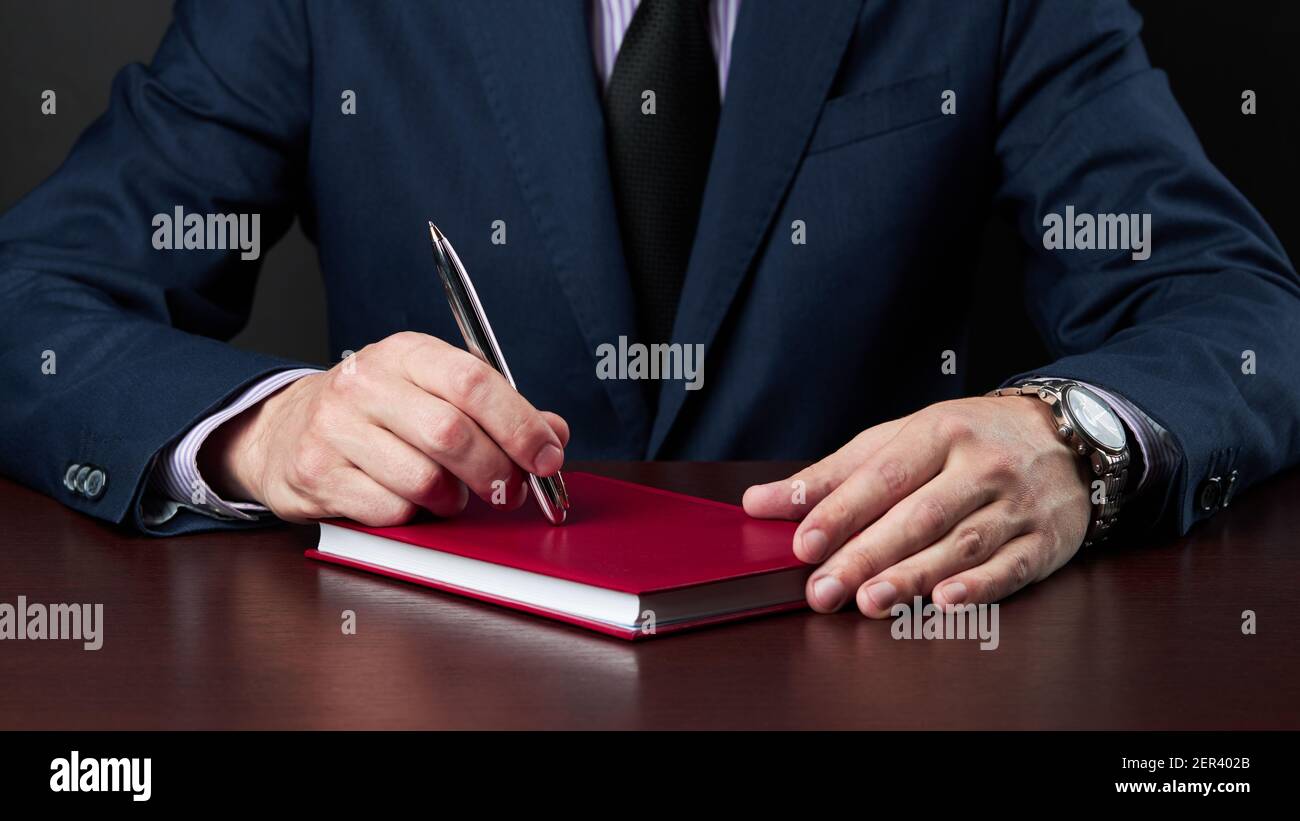 el hombre de negocios en el trabajo formal se sienta en el escritorio y sostiene un bolígrafo de plata en el brazo Foto de stock
