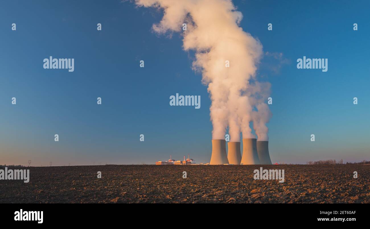 Temelin, república Checa - 02 28 2021: Central nuclear Temelin, torres de refrigeración al vapor en el paisaje al atardecer, campo en primer plano Foto de stock